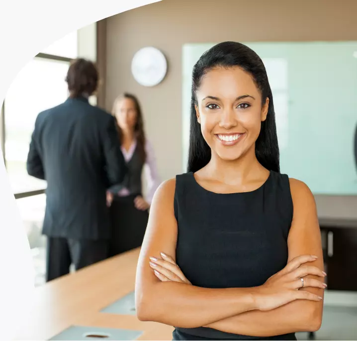 Uma mulher morena sorrindo em pé em uma sala de reunião.