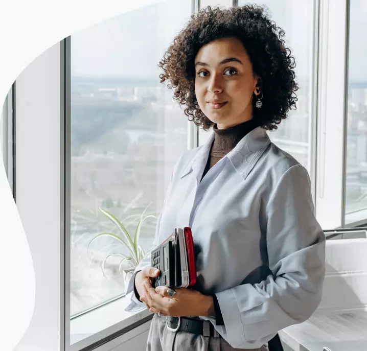 Uma mulher em frente a janela com livros em sua mão vestida de terno.